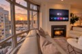Living room with oversized curved windows showing a marina and sunset, beige sofa, and a fireplace with a wall-mounted TV above it