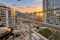 View from a high-rise balcony overlooking a cityscape at sunset, with string lights along the railing in the foreground.