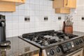 Stainless steel gas stove on a dark granite countertop with a knife block to the right and a coffee machine to the left against a white tile backsplash.
