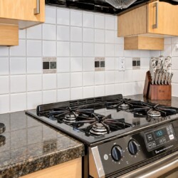 Stainless steel gas stove on a dark granite countertop with a knife block to the right and a coffee machine to the left against a white tile backsplash.