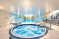 Indoor spa facility with a round bubbling hot tub in the foreground and a rectangular pool beyond.