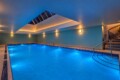 Indoor pool area with bright blue water, blue walls, and a skylight in the ceiling; warm wall and ceiling lighting creates a spa-like ambiance.