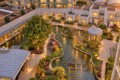 Aerial view of a modern apartment complex with a winding canal, landscaped gardens, and warm indoor lights at dusk, viewed from above.