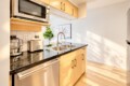 Modern kitchen with black granite countertop, double sink, and stainless steel appliances under light wood cabinets.