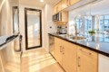 Modern kitchen with light wood cabinets, stainless steel appliances, and a double sink facing a bright living area.