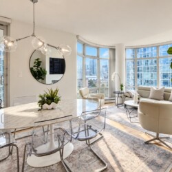 Open-plan living and dining area with a marble dining table, clear acrylic chairs, curved bay windows, and an urban cityscape outside.