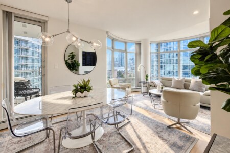 Open-plan living and dining area with a marble dining table, clear acrylic chairs, curved bay windows, and an urban cityscape outside.