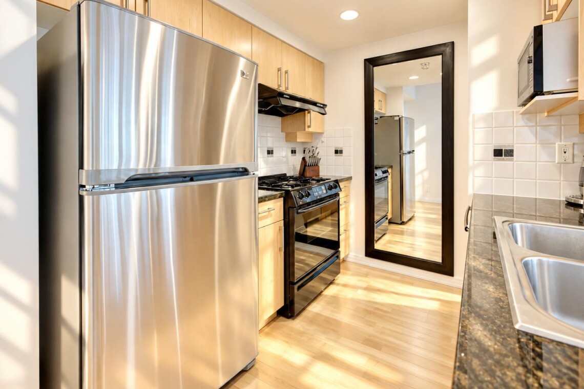 Modern kitchen with stainless steel refrigerator, gas range, and microwave, light wood cabinets, and granite countertops.