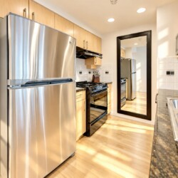 Modern kitchen with stainless steel refrigerator, gas range, and microwave, light wood cabinets, and granite countertops.