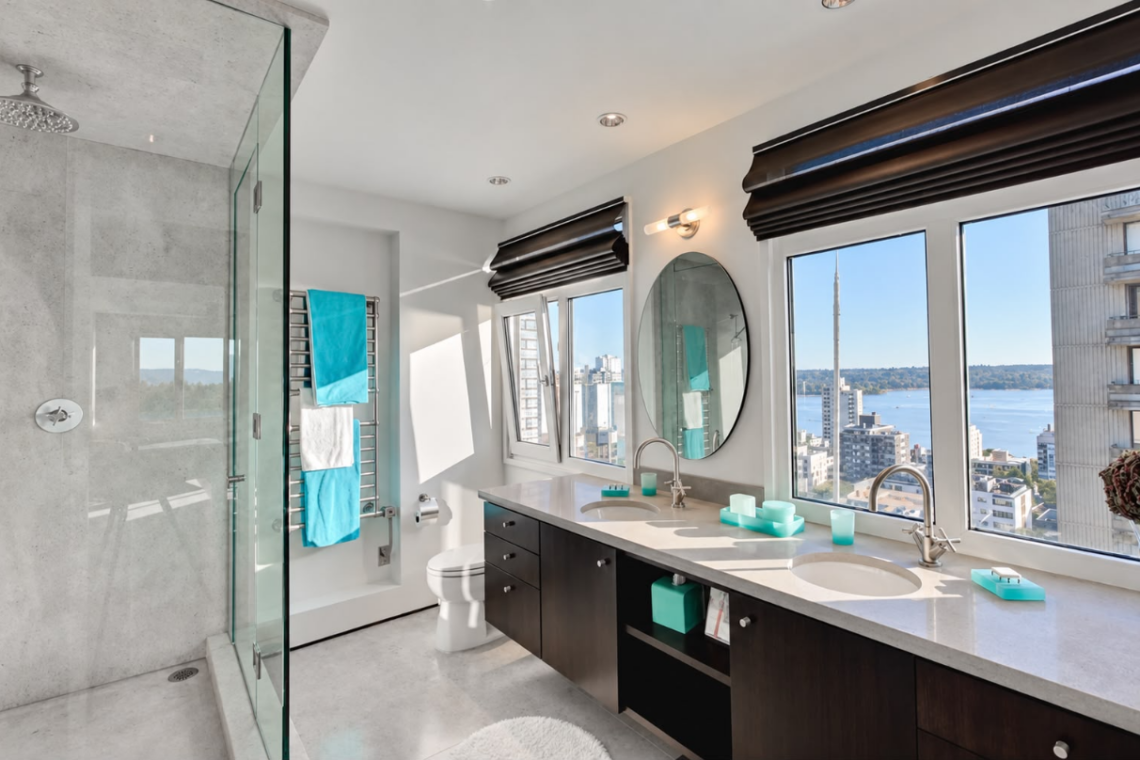 Modern bathroom with double sinks, black cabinets, and a wide window view of the city and water.
