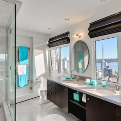 Modern bathroom with double sinks, black cabinets, and a wide window view of the city and water.