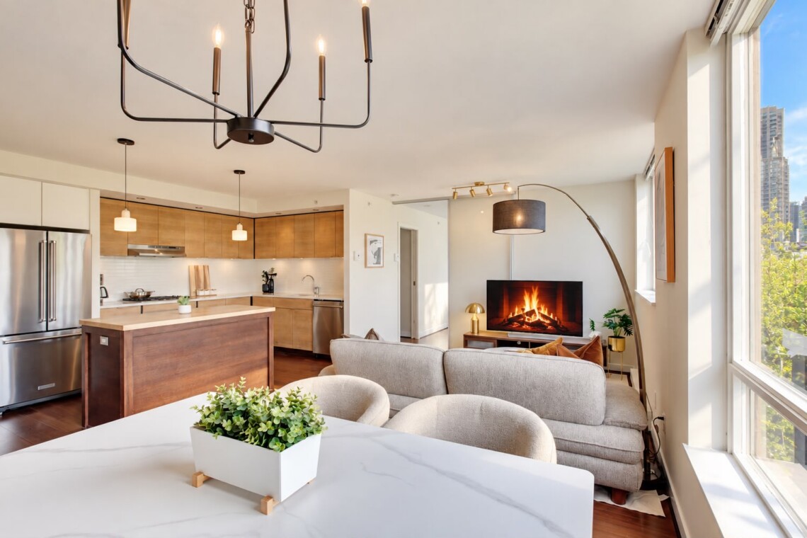 Open-concept living space with a wooden-kitchen island, stainless steel appliances, and a gray sofa facing a fireplace TV.