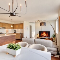 Open-concept living space with a wooden-kitchen island, stainless steel appliances, and a gray sofa facing a fireplace TV.