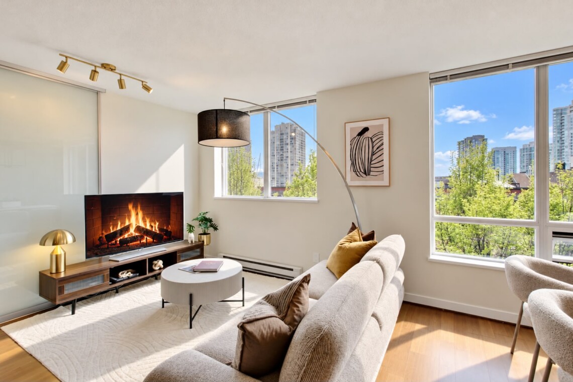 Cozy modern living room with a gas fireplace, beige sofa, and large windows overlooking a city skyline.
