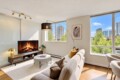 Cozy modern living room with a gas fireplace, beige sofa, and large windows overlooking a city skyline.