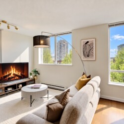 Cozy modern living room with a gas fireplace, beige sofa, and large windows overlooking a city skyline.