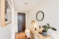 Modern entryway with a wooden console table, round black-framed mirror, amber glass lamp, and a potted plant beside the front door.