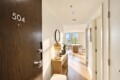 Apartment entry hallway with a dark wood door marked 504, a wooden console, round mirror, and warm lamp.