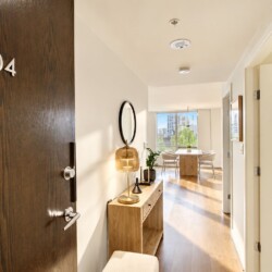 Apartment entry hallway with a dark wood door marked 504, a wooden console, round mirror, and warm lamp.