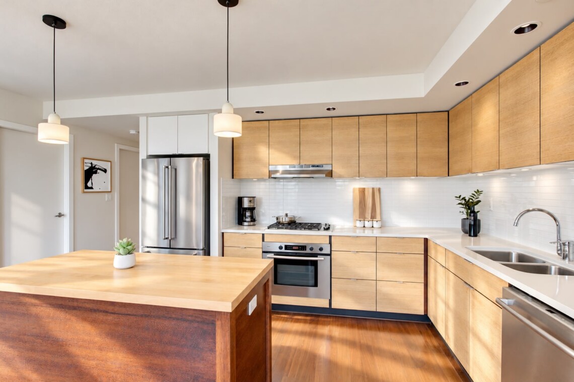 Bright modern kitchen with wooden cabinets, stainless steel appliances, and a large island in the foreground