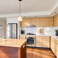 Bright modern kitchen with wooden cabinets, stainless steel appliances, and a large island in the foreground