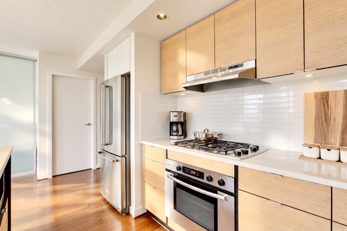 Modern kitchen with stainless steel refrigerator, gas range, and light wood cabinets, white tile backsplash, and wooden cutting boards on the counter