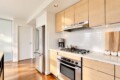 Modern kitchen with stainless steel refrigerator, gas range, and light wood cabinets, white tile backsplash, and wooden cutting boards on the counter