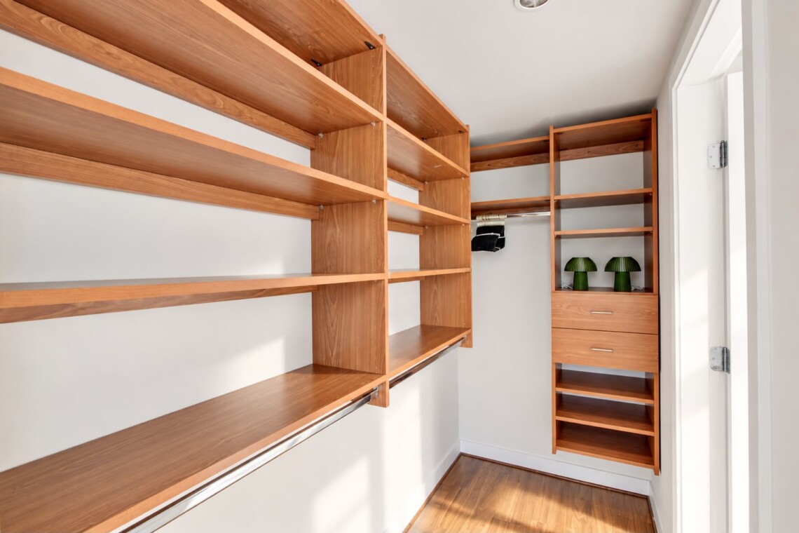 Walk-in closet with warm wooden shelving, a hanging rod, and a tall drawer cabinet; two green lamps on the shelf.