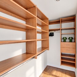 Walk-in closet with warm wooden shelving, a hanging rod, and a tall drawer cabinet; two green lamps on the shelf.