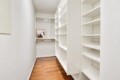 A small walk-in closet with white shelves and a wooden floor; a framed black-and-white photo sits on a clothing rod at the back wall.