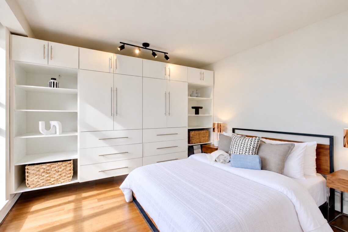 Modern bedroom with a large white built-in wardrobe system along the wall beside a neatly made bed.