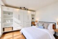 Modern bedroom with a large white built-in wardrobe system along the wall beside a neatly made bed.
