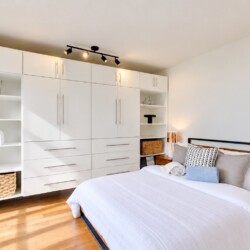 Modern bedroom with a large white built-in wardrobe system along the wall beside a neatly made bed.