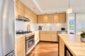 Modern L-shaped kitchen with light wood cabinets, stainless appliances, and a large central island.