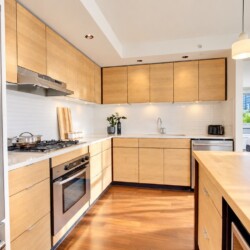 Modern L-shaped kitchen with light wood cabinets, stainless appliances, and a large central island.
