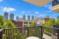 Balcony view of a city with a colorful mural, green trees, and string lights along a black railing.