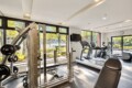Well-lit gym with a multi-station weight machine in the foreground and treadmills by large windows overlooking trees outside. - Informative image with equipment layout.