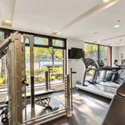 Well-lit gym with a multi-station weight machine in the foreground and treadmills by large windows overlooking trees outside. - Informative image with equipment layout.