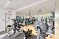 Bright gym interior with cardio machines (stationary bikes and elliptical) in foreground and a wall of mirrors, exercise balls, and weights in background