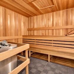 Wood-paneled sauna interior with two-tier benches and a metal heater filled with rocks on the left.