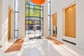 Bright modern lobby with tall glass doors and white walls; orange brick floor mats and wooden wall niches flank the entryway outside view through doors