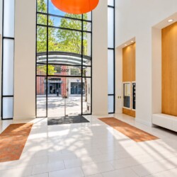 Bright modern lobby with tall glass doors and white walls; orange brick floor mats and wooden wall niches flank the entryway outside view through doors