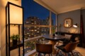 Cozy urban balcony dining nook at dusk with a round wooden table, four mid-century chairs, and warm lamps overlooking city lights.