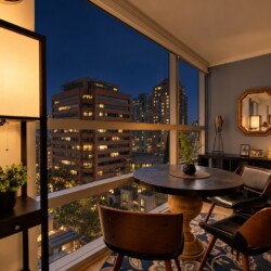 Cozy urban balcony dining nook at dusk with a round wooden table, four mid-century chairs, and warm lamps overlooking city lights.