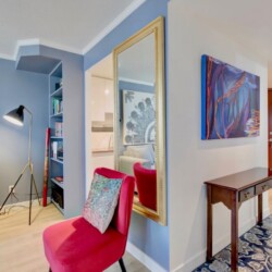 Cozy living area with blue walls, gray sofa, black floor lamp, a red accent chair, and a gold-framed mirror.