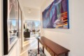 Narrow hallway opening to a bright living area with a large abstract painting on the right and a wooden console table with brass handles.