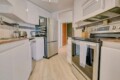 Modern galley kitchen with white cabinets and stainless steel appliances, including fridge, oven, microwave, and dishwasher; a knife block and toaster on the counter.