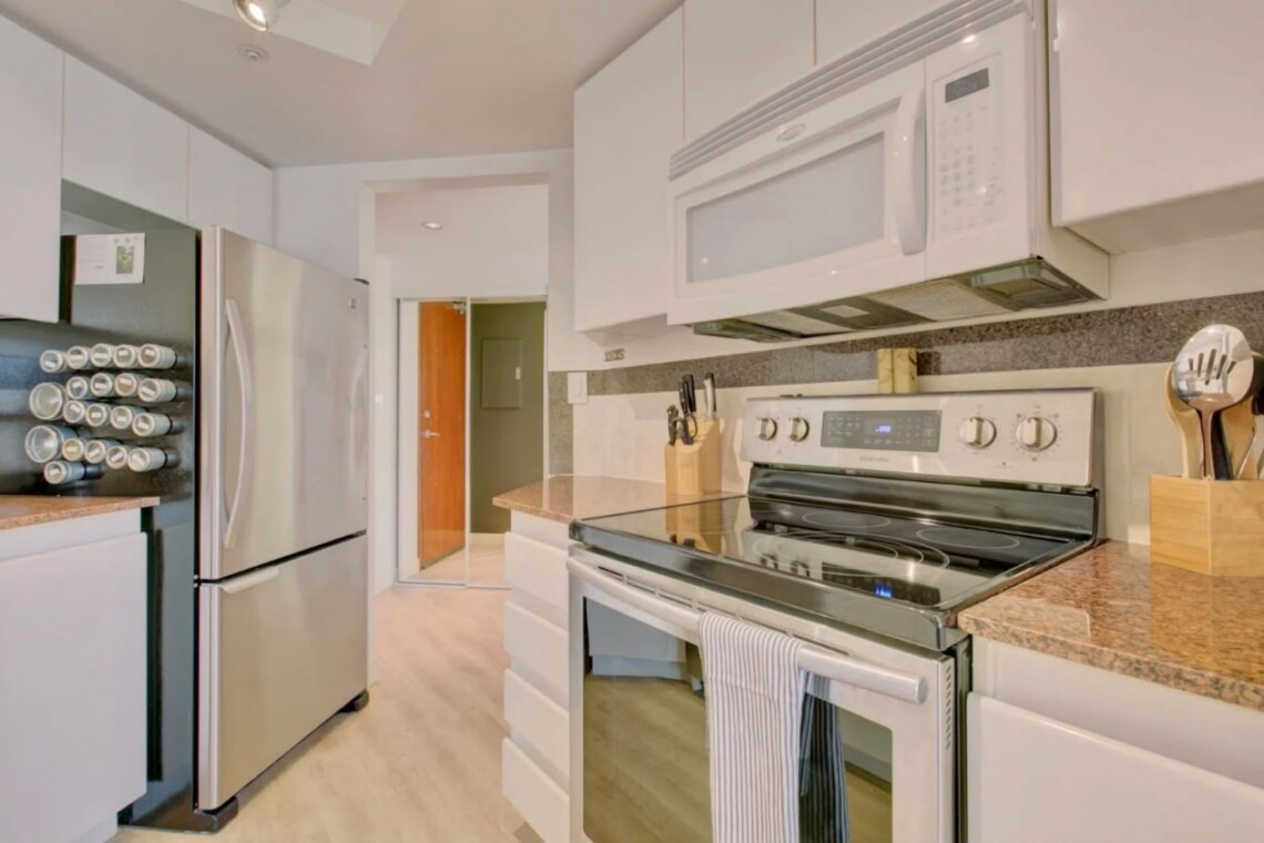 Modern kitchen with stainless steel refrigerator, microwave, and stove, white cabinets, and speckled countertops.