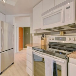 Modern kitchen with stainless steel refrigerator, microwave, and stove, white cabinets, and speckled countertops.