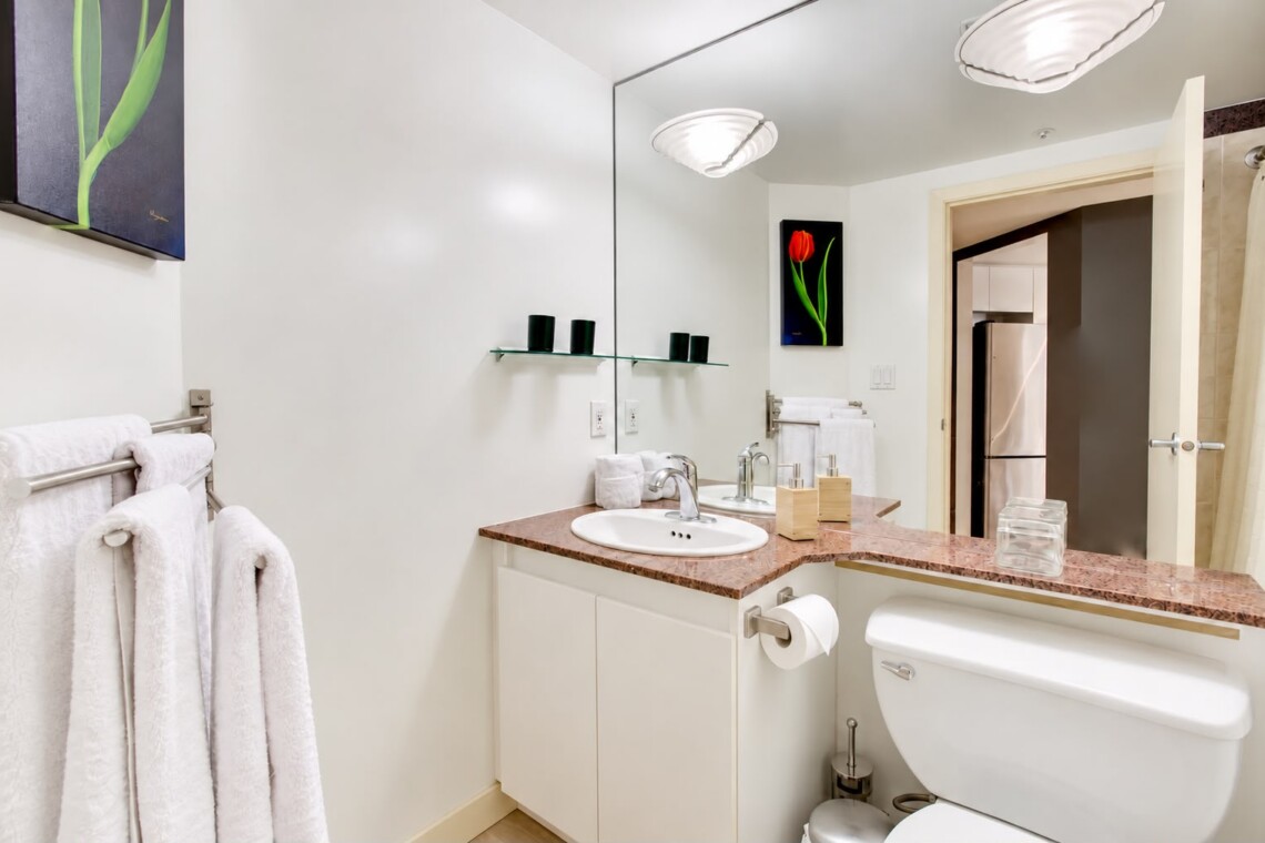 Modern bathroom with white vanity, marble countertop, and large mirror reflecting a towel rack and tulip artwork above the sink area.